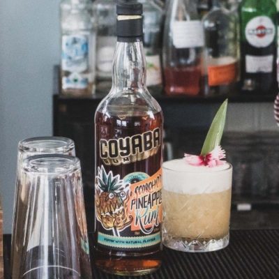 Coyaba Scorched Pineapple rum bottle on a bar next to a fruity cocktail