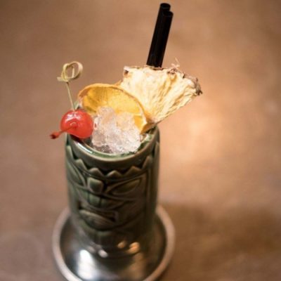 Coyaba Scorched Pineapple rum cocktail in a ceramic tiki jar with a cherry and dried pineapple garnish