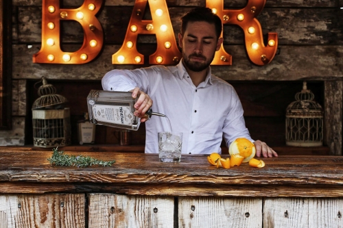 Trevethan Distillery - a bartender pouring a cocktail behind a wooden bar with rosemary and orange peel
