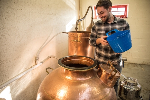Trevethan Distillery - man looking into a still with a blue bucket