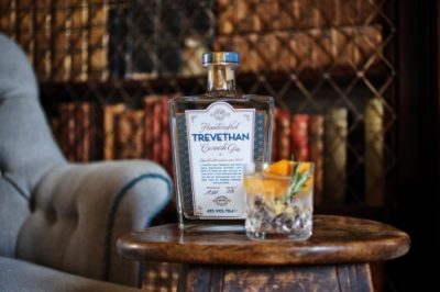 Trevethan Gin bottle and cocktail in a tumbler on a dark wooden table in front of a blurry bookcase