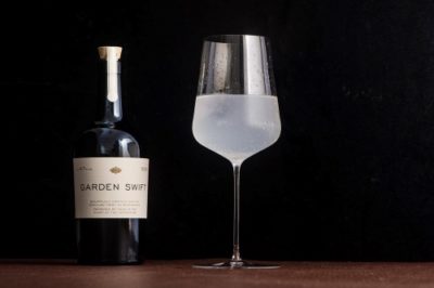 Garden Swift Dry Gin bottle next to a wine glass with eaux de vie liquid on a dark backdrop
