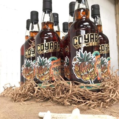 Several bottles of Coyaba Scorched PIneapple Rum in nest of shredded brown paper on hessian
