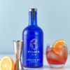 6 O Clock Gin bottle next to a negroni cocktail, jigger and a slice of orange