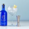 6 O Clock Gin bottle on a white surface next to a gin goblet and a silver jigger