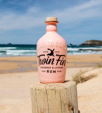 Twin Fin Coconut and Lychee Rum bottle on a beach on a large wooden Groyne
