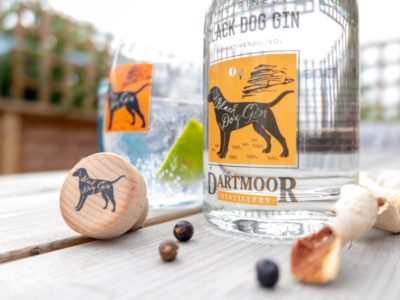 Black Dog gin bottle on a table with the cork top, juniper berries and orange peel