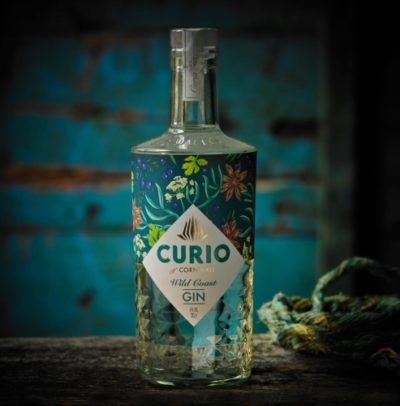 Curio Wild Coast Gin bottle on a dark wooden surface with a grunge, teal background