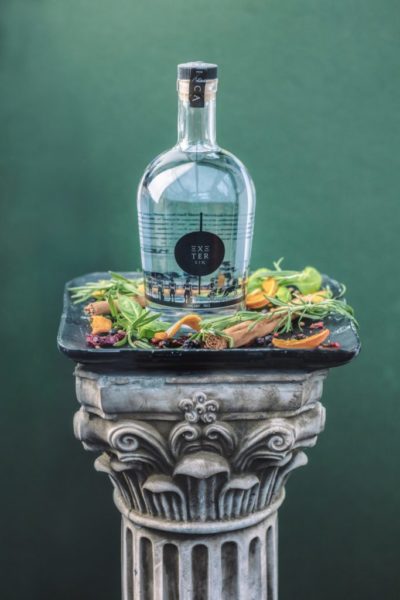 Exeter Gin bottle on a tray of botanicals on a Roman pillar