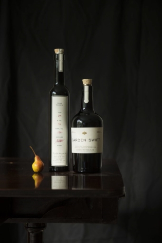 Garden Swift Dry Gin bottle next to a bottle of eaux de vie and a pear on a dark table