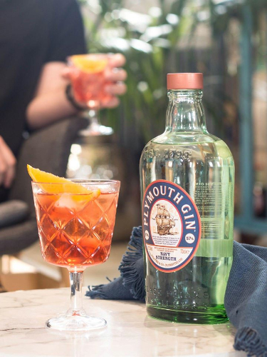 Plymoth Gin bottle next to a Negroni cocktail with a person blurred in the background