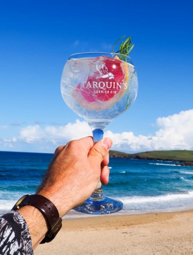 Tarquins Dry Gin in a gin goblet with a slice of grapefruit being held up in fromt of a beach
