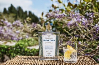 Trevethan Gin bottle on a wicker basket next to a tumbler in front or a blurred floral background