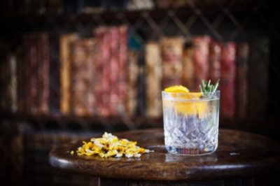 Trevethan Gin cocktail in a tumbler on a dark wooden table in front of a blurry bookcase