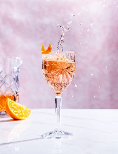 Salcombe Gin 'Rose Sainte Marie' cocktail in a glass in front of a pink background with and orange wedge