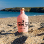 Twin Fin Coconut and Lychee Rum bottle on the sand with the sea in the background